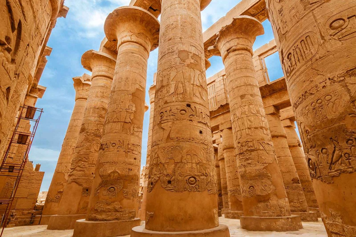 Tall sandstone columns covered with hieroglyphs and Egyptian figures in Karnak Templeโs hypostyle hall