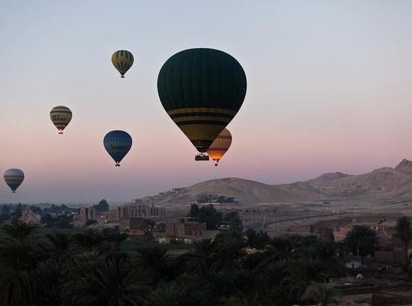 Hot air balloons floating above palm trees, fields and desert hills on Luxor’s west bank at dawn