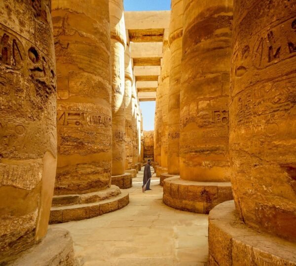 A visitor walking between massive hieroglyph-covered columns in the hypostyle hall at Karnak Temple