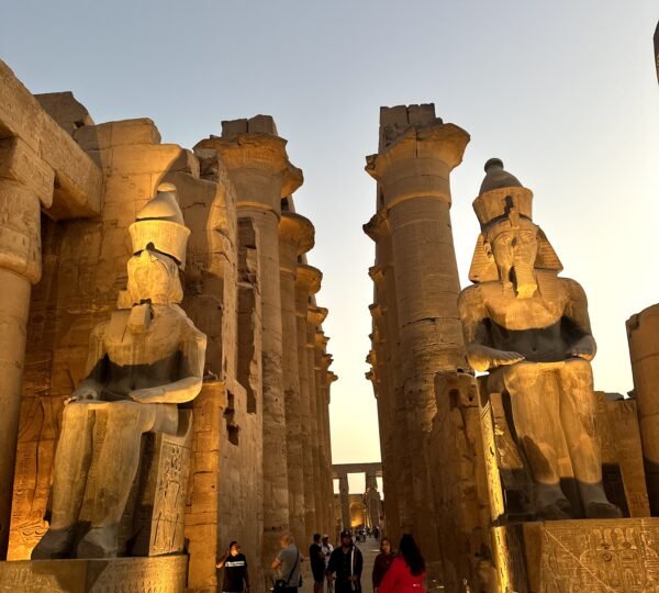 Visitors walking between illuminated statues and columns at Luxor Temple at dusk