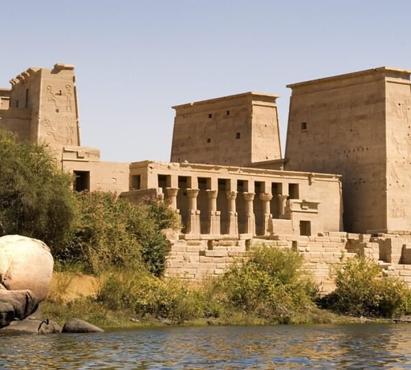 Philae Temple rising above rocks, shrubs and the blue waters of the Nile