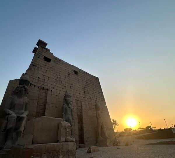 Sun setting beside the stone pylon and statues of Luxor Temple