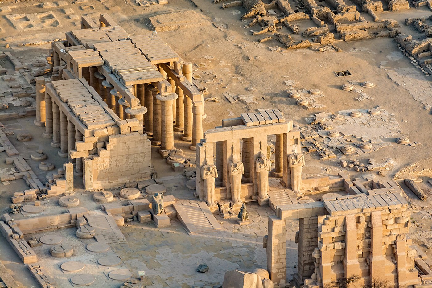 An aerial view of ancient temple colonnades, standing statues, stone gateways and surrounding excavated ruins in Luxor