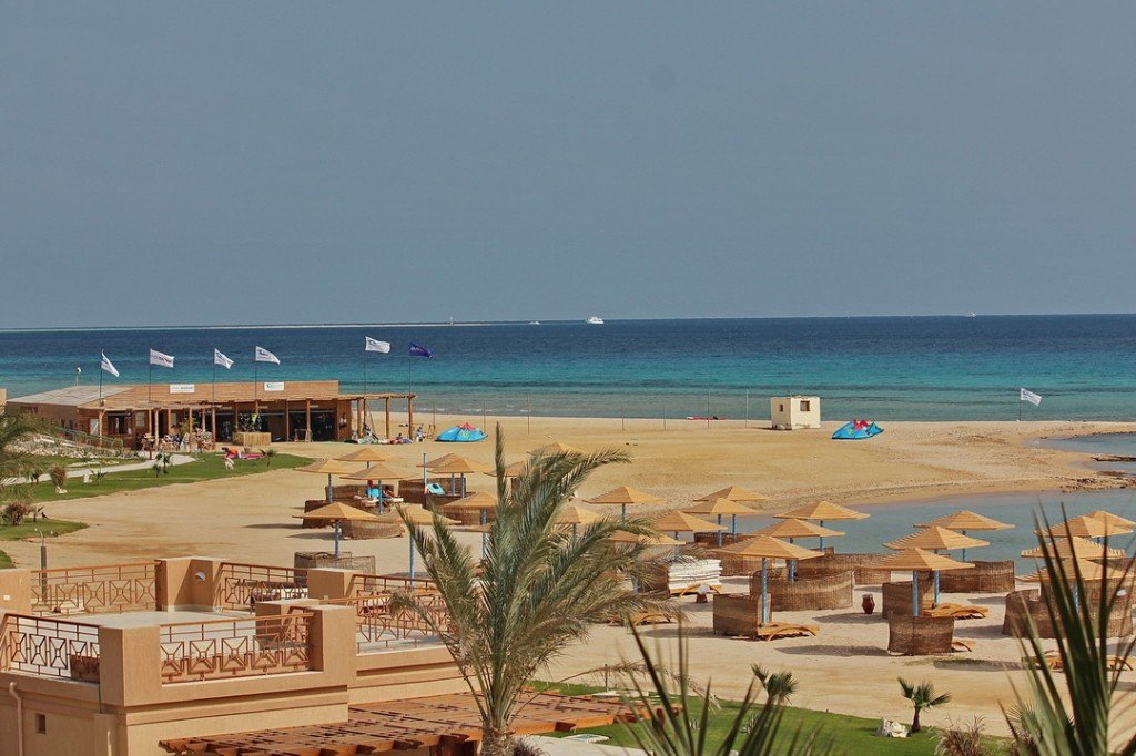 Beach umbrellas, palm trees and resort buildings beside a sandy beach and turquoise Red Sea water