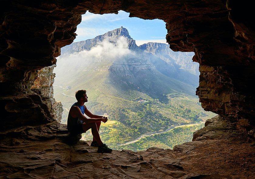 Hiker resting in a cave above a mountain valley