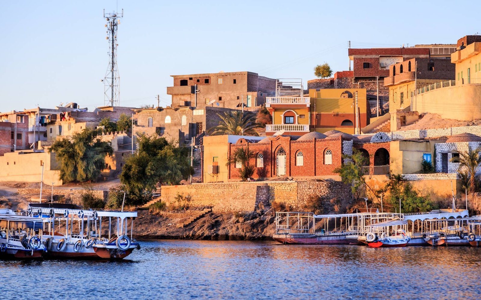 Colorful Nubian houses on a hillside above passenger boats moored along the Nile in Aswan