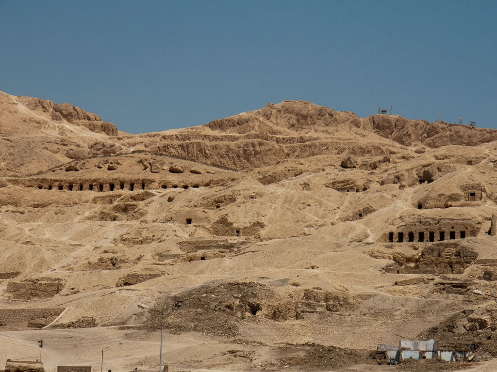 Rows of dark rock-cut tomb openings across a dry limestone hillside in Luxor