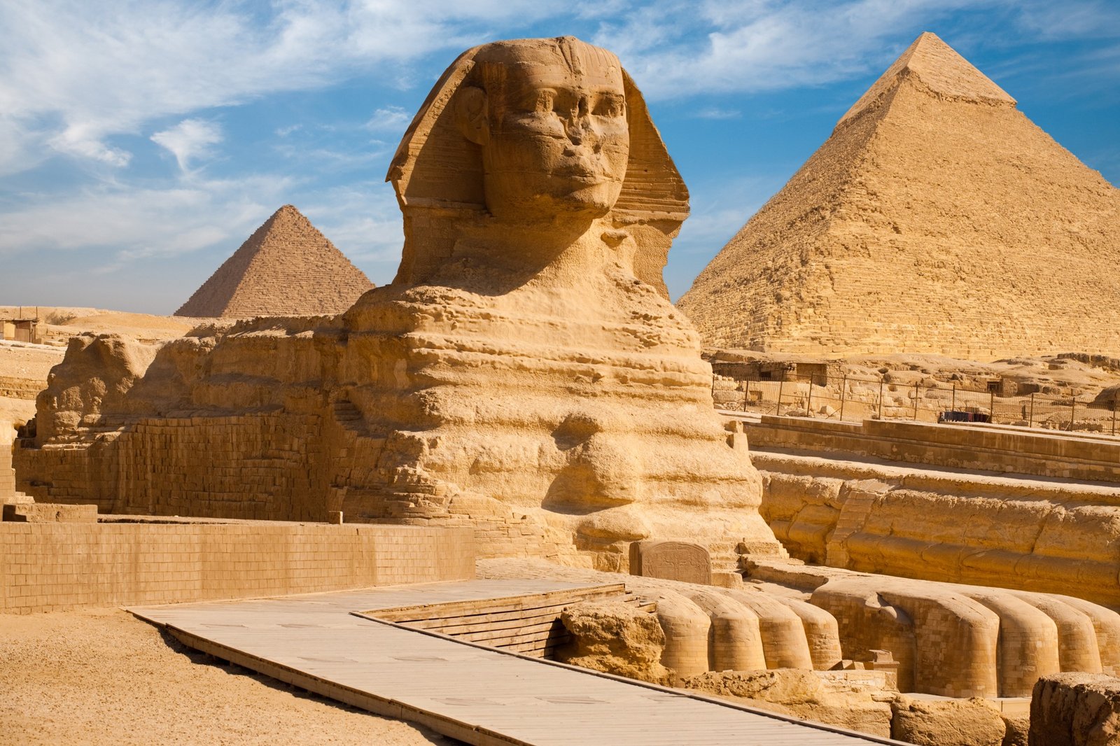 The Great Sphinx of Giza in the foreground with two pyramids behind beneath a blue sky