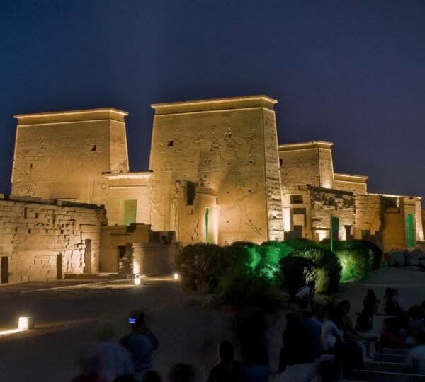 Seated visitors watching the illuminated pylons of Philae Temple during the nighttime sound and light show