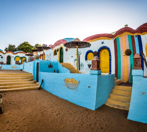 Steps and sandy paths between blue-painted walls, colorful doors and traditional domed Nubian buildings