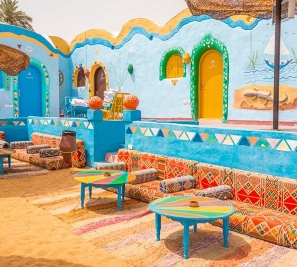 Patterned cushioned benches and painted tables in a courtyard with blue walls and bright arched doors