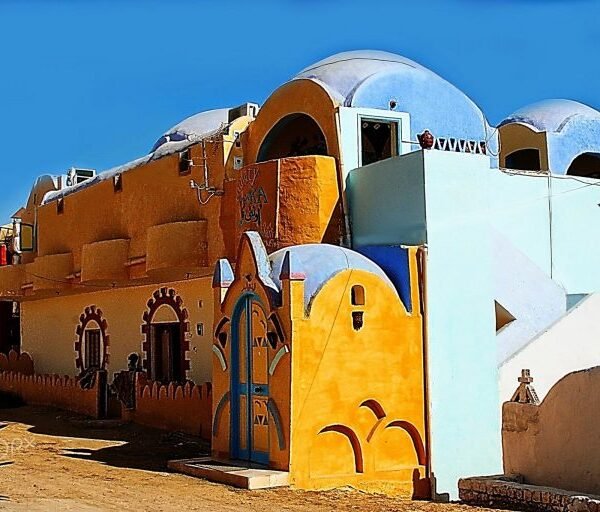 Orange, yellow and pale blue Nubian houses with rounded roofs and decorated doorways beneath a clear sky