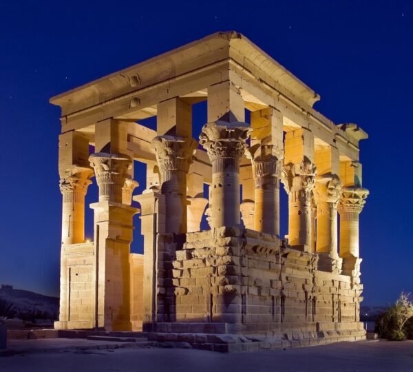The columns and stone lintels of Trajan’s Kiosk at Philae lit in gold beneath a deep blue evening sky