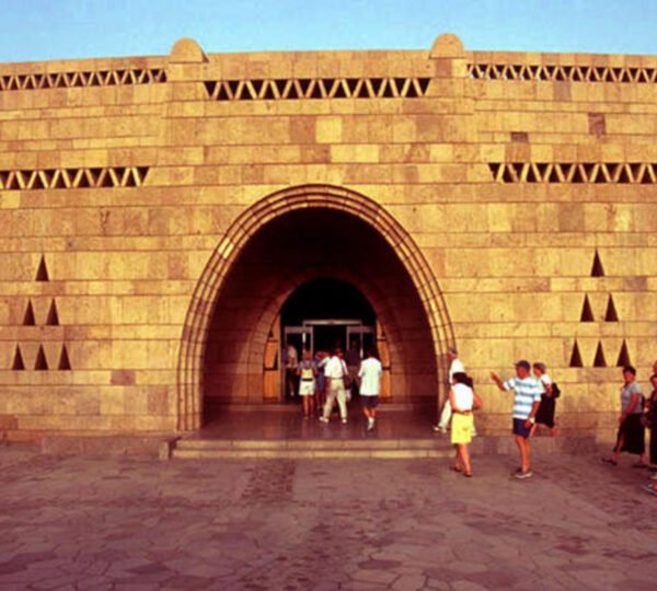 Visitors outside the arched entrance of the Nubian Museum, beneath its patterned stone facade
