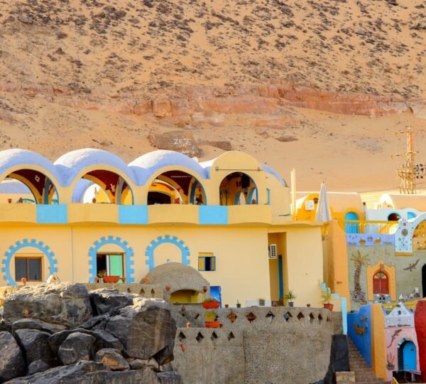 A yellow Nubian house with blue arches, colorful gateways and rocky desert hills behind