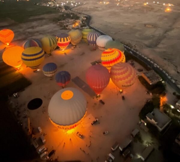 An aerial view of colorful balloons glowing from their burners on the launch field before dawn in Luxor