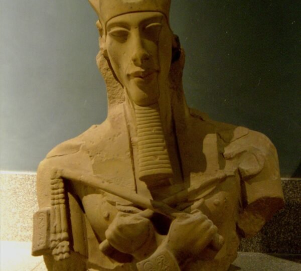 A fragmentary ancient Egyptian royal bust with crossed arms, a long ceremonial beard and a carved headdress