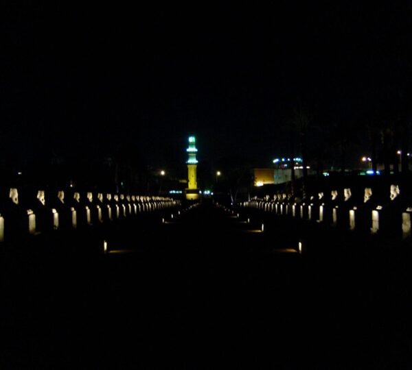 Two long rows of illuminated sphinx statues leading toward a lit minaret in Luxor at night
