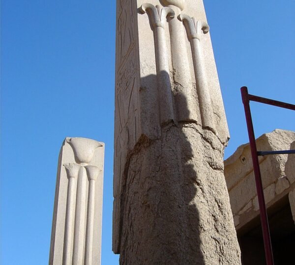 Tall stone pillars decorated with raised papyrus forms beneath a clear blue sky at Karnak Temple