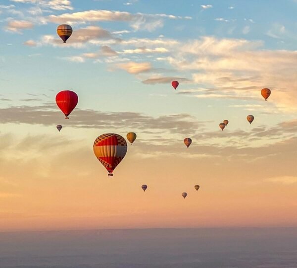Colorful hot air balloons scattered across a cloud-dappled dawn sky above the Luxor landscape