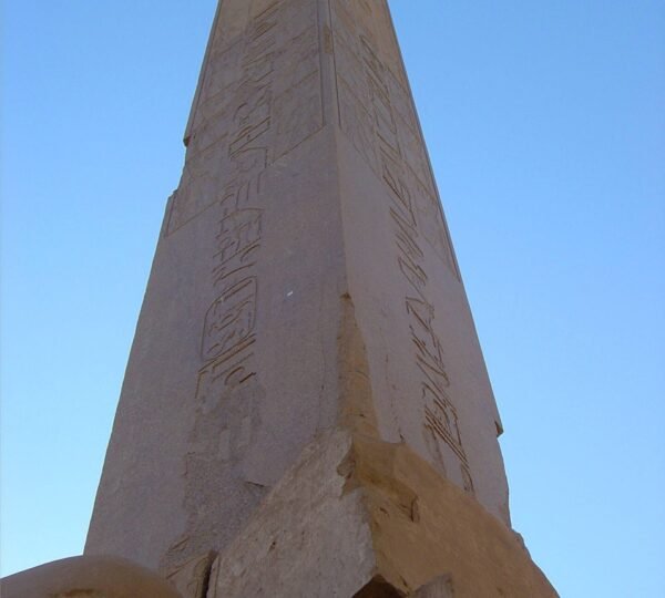 An upward view of a stone obelisk covered with hieroglyphs against a clear blue sky at Karnak