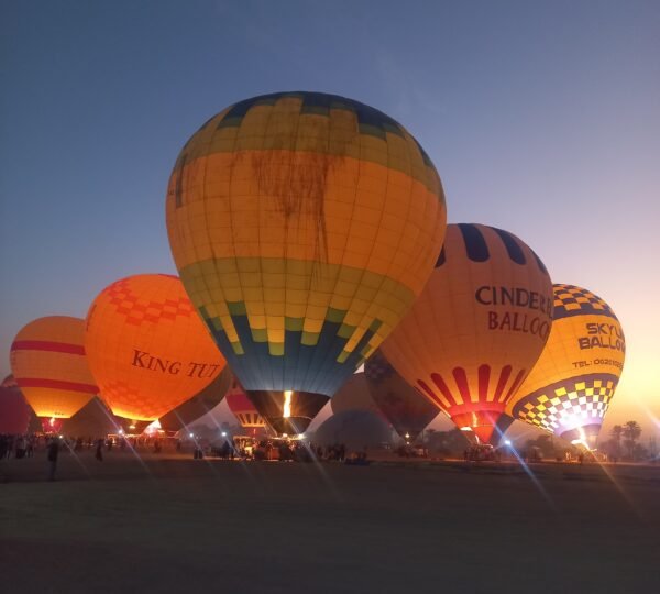 Colorful hot air balloons being inflated by glowing burners before dawn in Luxor