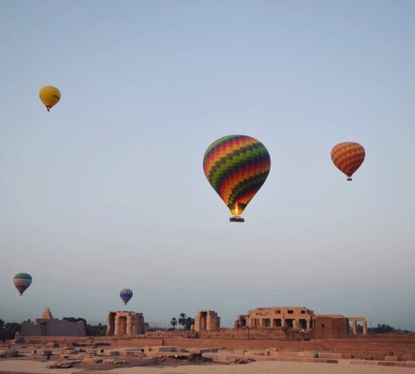 Colorful balloons floating above the stone remains and columns of an ancient temple on Luxorโs west bank
