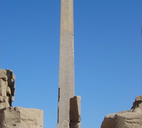 A tall hieroglyph-covered obelisk rising above broken columns and stone walls at Karnak Temple