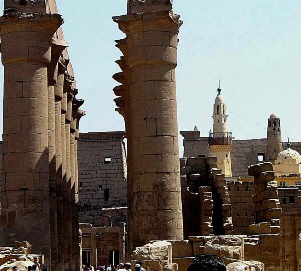 Visitors walking among the tall columns of Luxor Temple with Abu Haggag Mosque’s minarets behind