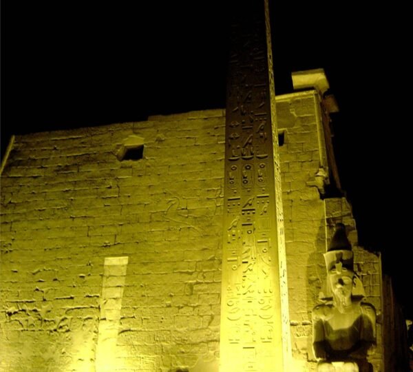 The hieroglyph-carved obelisk and a seated statue at Luxor Temple lit in gold after dark