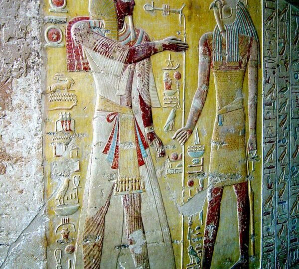 A painted pharaoh facing a falcon-headed figure on a yellow tomb wall bordered with hieroglyphs