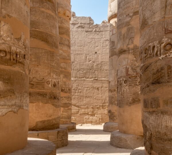 Sunlight falling between large hieroglyph-covered columns and a carved wall in Karnak Temple’s hypostyle hall