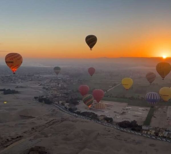Many colorful hot air balloons above fields and desert roads as the sun rises over Luxor