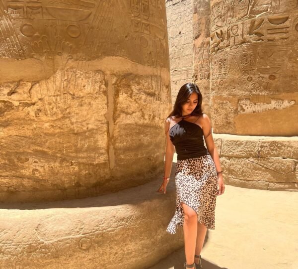 A traveler standing beside a large sandstone column covered with Egyptian figures and hieroglyphs at Karnak