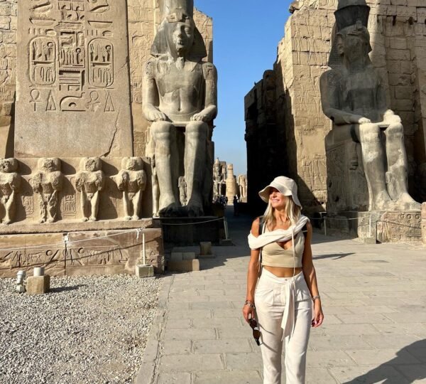 A traveler walking beside Luxor Temple’s hieroglyph-carved obelisk and seated entrance statues