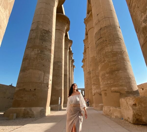 A traveler walking beneath tall sandstone columns in the colonnade of Luxor Temple
