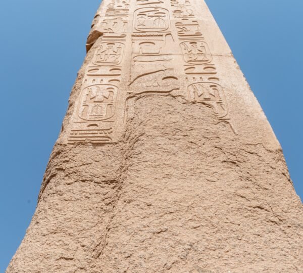 An upward close-up of hieroglyphs carved along a stone obelisk against a blue sky at Karnak