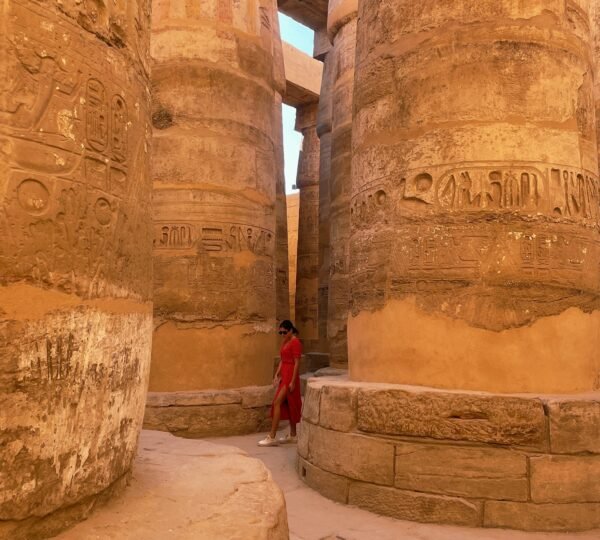 A visitor in red walking among massive carved sandstone columns at Karnak Temple