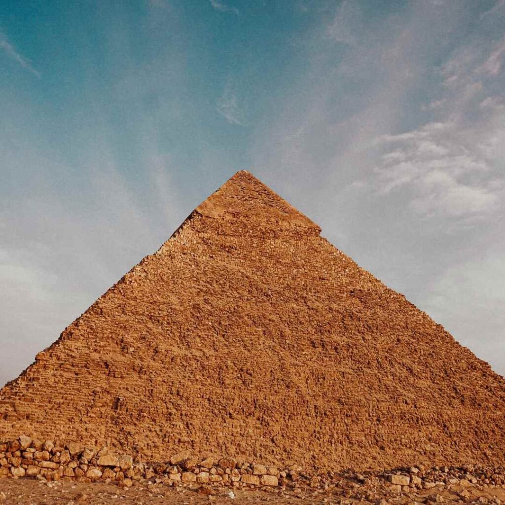 The stone-block face and pointed summit of a Giza pyramid beneath a pale blue sky