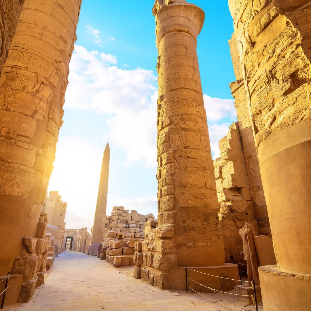 Carved sandstone columns framing a distant obelisk and ancient masonry at Karnak Temple in warm sunlight