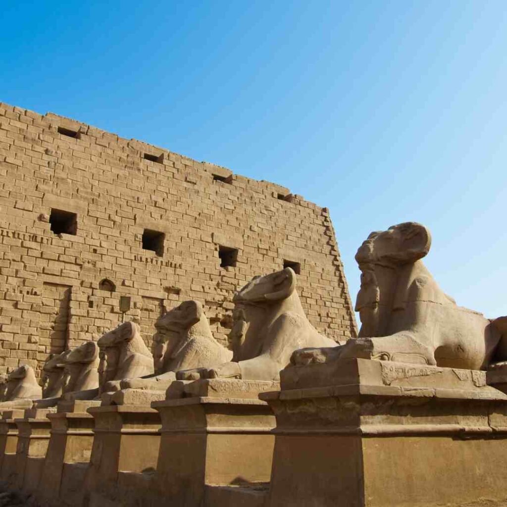 A row of ram-headed sphinxes on stone pedestals before the monumental entrance pylon at Karnak Temple