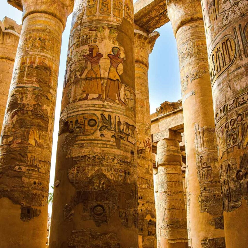 Massive temple columns covered with painted Egyptian figures and hieroglyphs at Karnak in Luxor