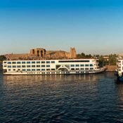 A white cruise ship with blue windows moored on the Nile beneath the ruins of Kom Ombo Temple