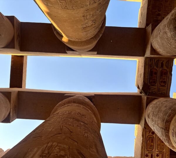 An upward view of massive carved columns and stone lintels framing the blue sky at Karnak Temple