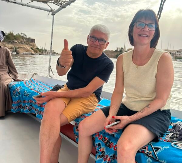 Two travelers seated on patterned cushions aboard a boat on the Nile in Aswan
